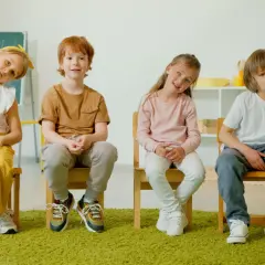 Cztery dzieci siedzą na krzesłach. Jedno z nich, z rudymi włosami, uśmiecha się, być może zmagając się z zaburzeniami neurorozwojowymi.