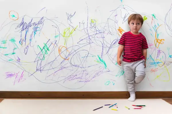 Chłopiec stoi przy ścianie pokrytej kolorowymi bazgrołami. Czy to oznaka, jak rozpoznać ADHD u dziecka?